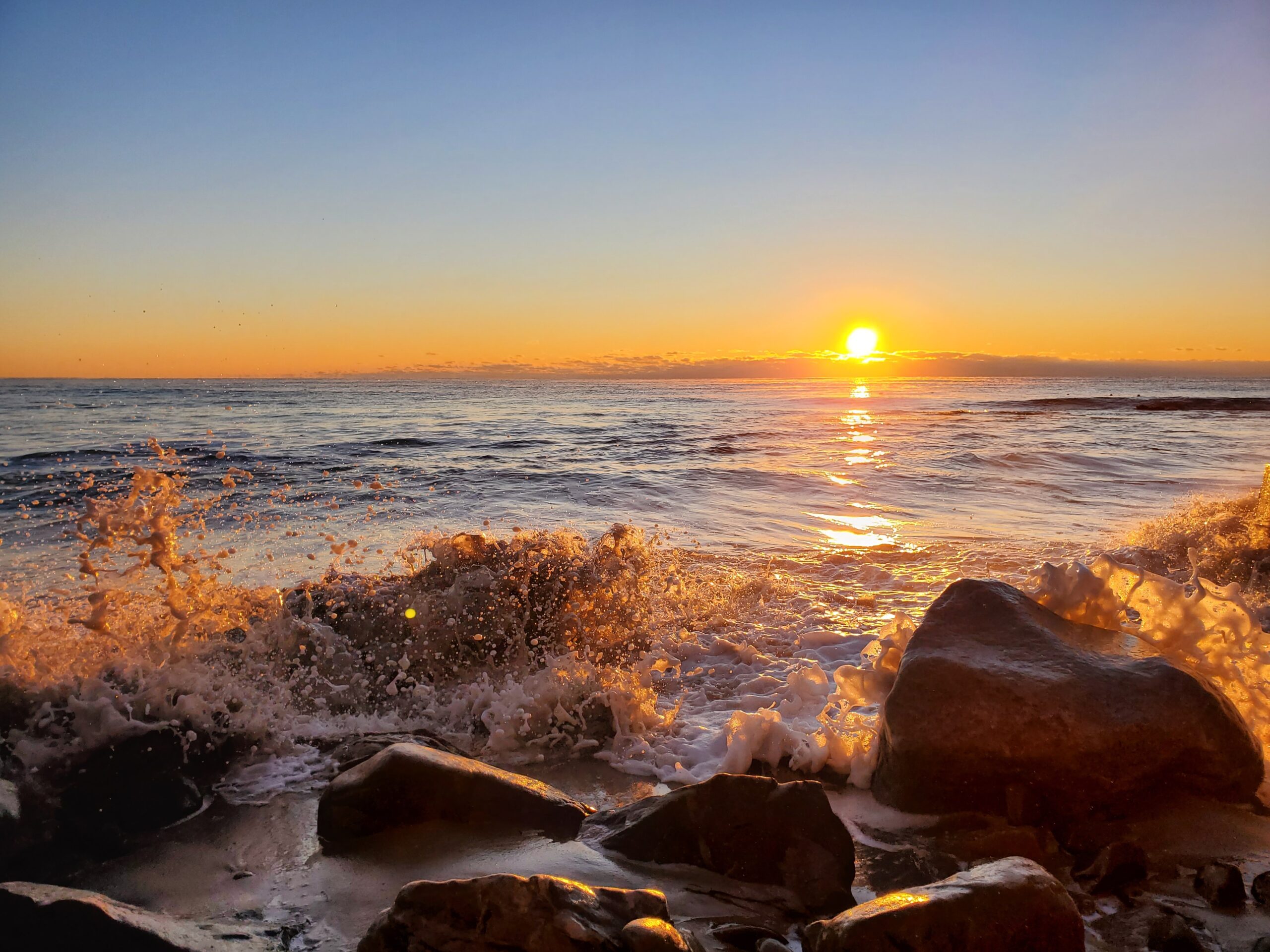 Sunset over ocean splashing into rocks